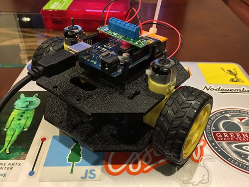 A small two-wheeled robot powered with an Arduino, on top of a laptop with many stickers.